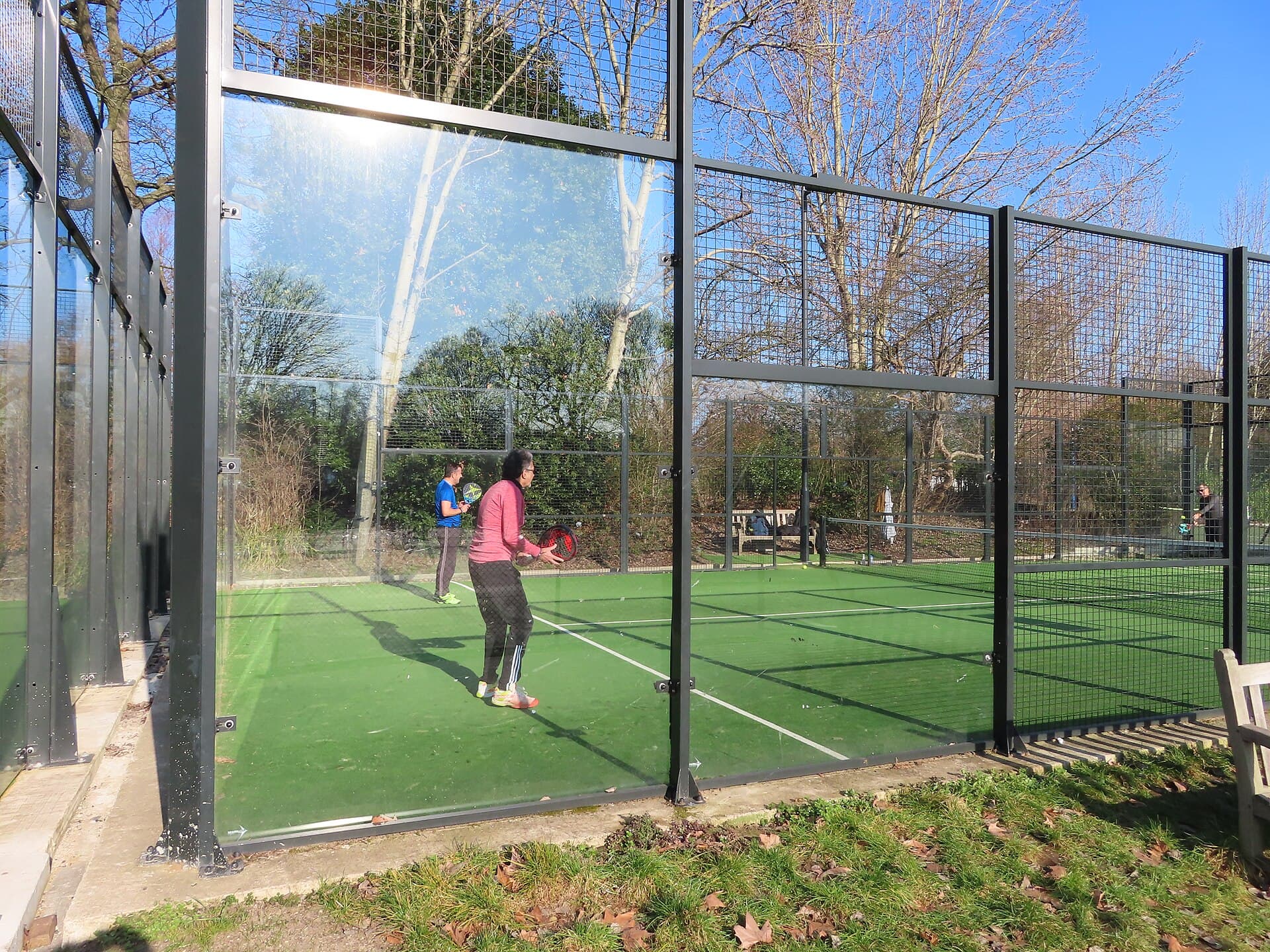 Padelbane med glasvægge og spillere i aktion